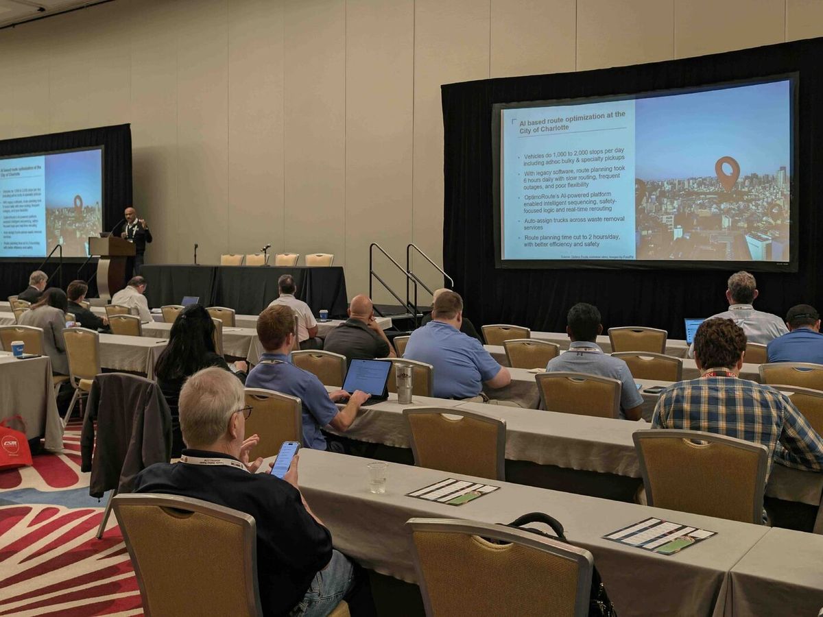 Ganes Kesari presenting to a seated audience, a slide on AI route optimization on screen