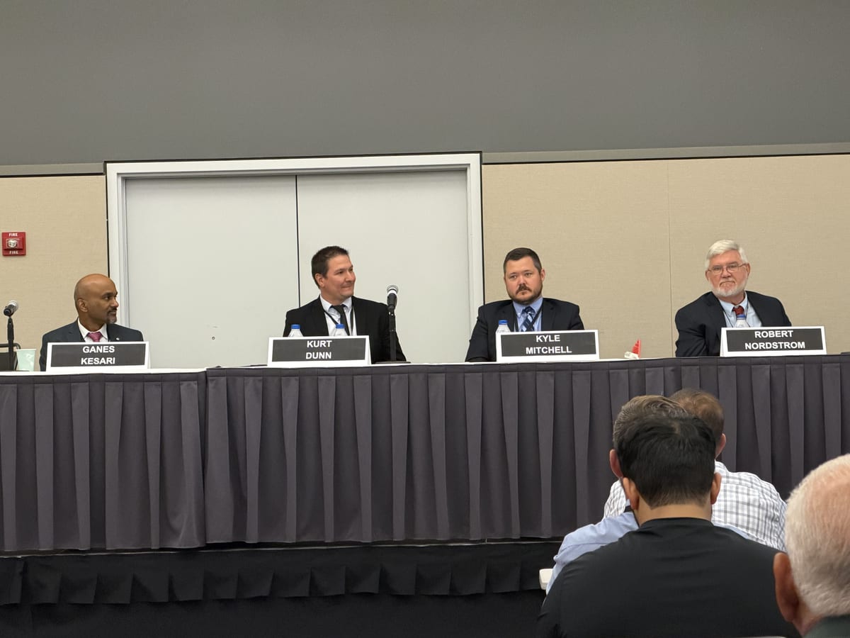 Ganes Kesari seated on a four-person panel at the TMC Fall Meeting, name cards on the table and the audience in the foreground