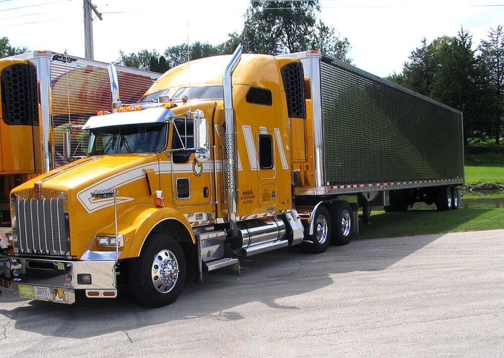 A yellow Brakebush Transportation Kenworth tractor and trailer parked at the yard